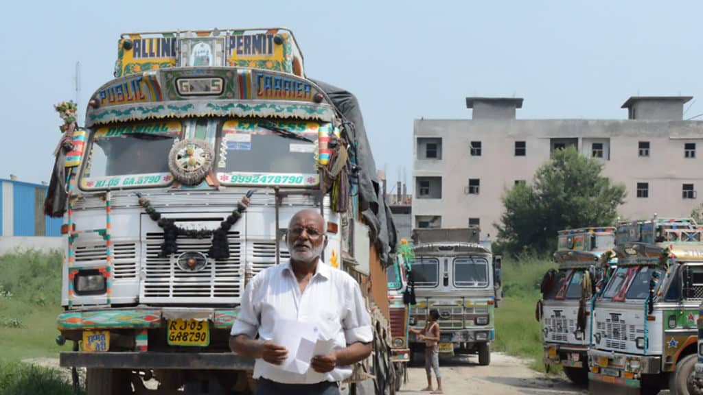 A truck driver stands in front of his colourful truck.