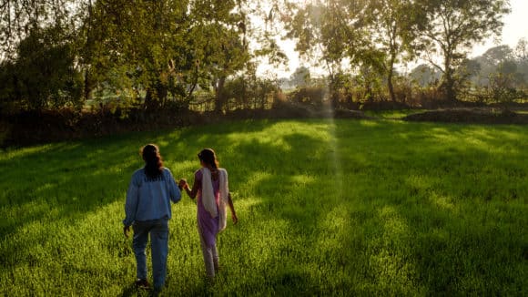 Two girls walk across grass.