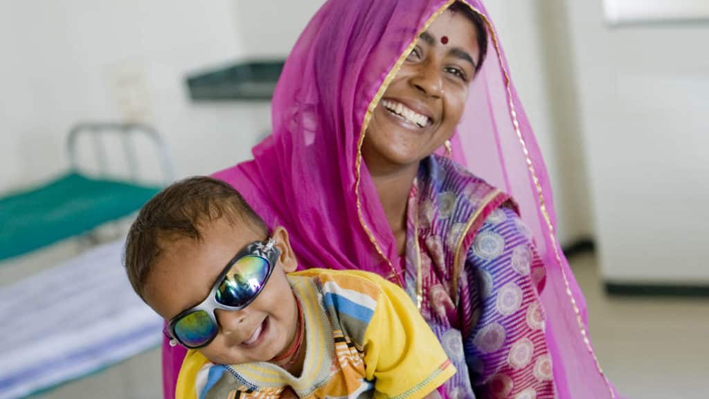 A young boy sit, smiling on his mother's lap.