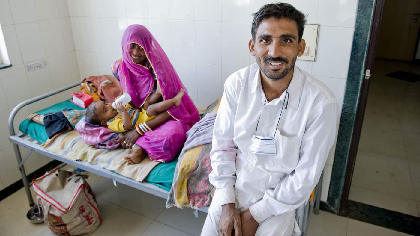 A young boy, lays on his mother's lap and his father sits smiling next to them.