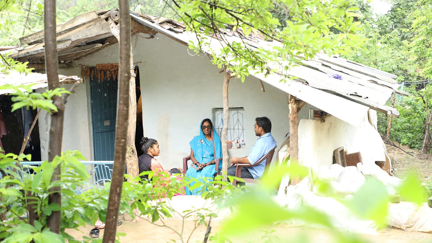 A lady sits outside her house with her grown up children.