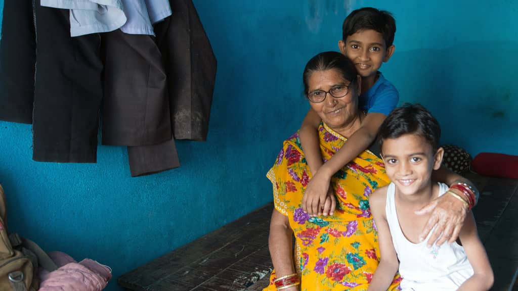 An older women sits on a bed, smiling with two of her grandsons.