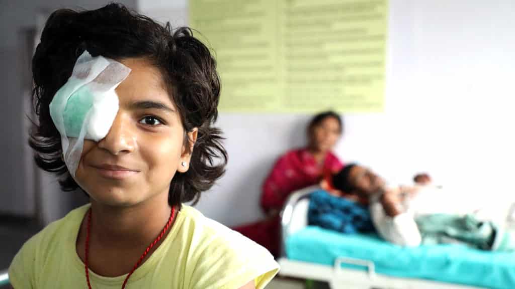 A girl smiling with an eye patch after cataract surgery.