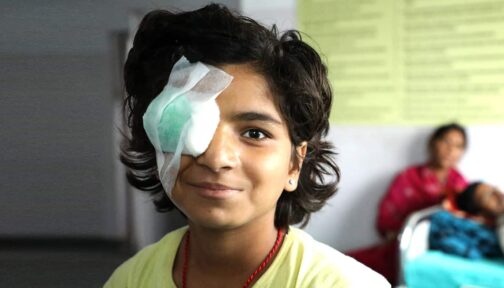 A girl smiling with an eye patch after cataract surgery.