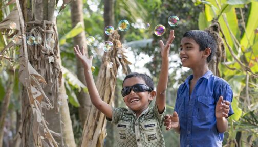 Two boys play with bubbles outside, one is wearing dark glasses.