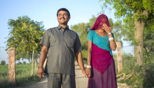 A man and women hold hands outside, smiling.