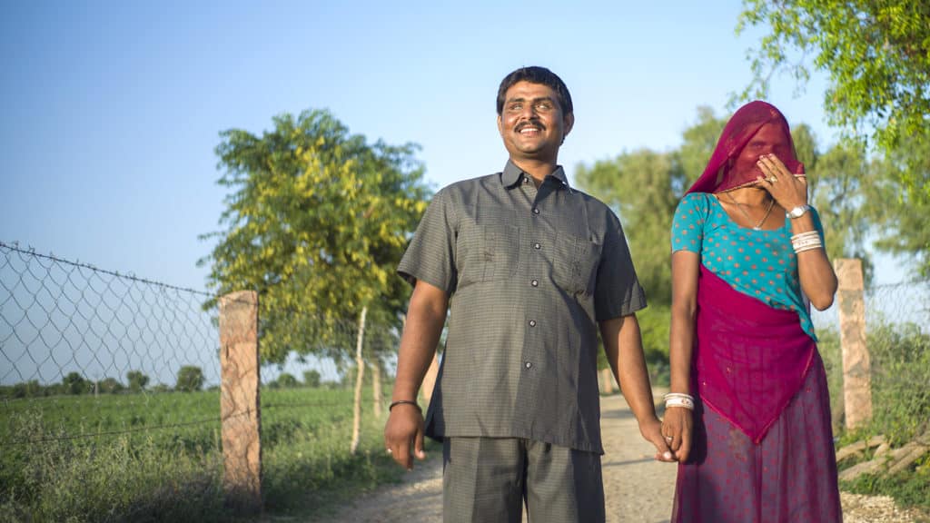 A man and women hold hands outside, smiling.