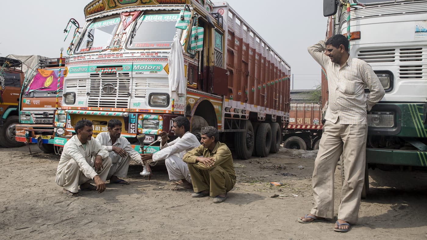 Indian truck drivers sit on the ground and relax in front of their trucks.