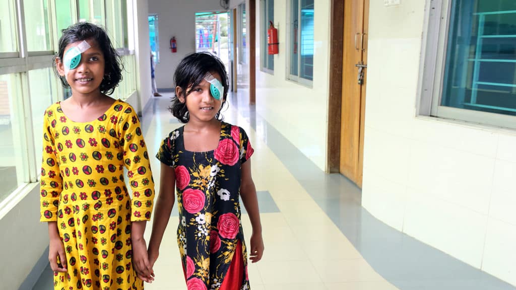 Two girls walk hand in hand after cataract surgery.