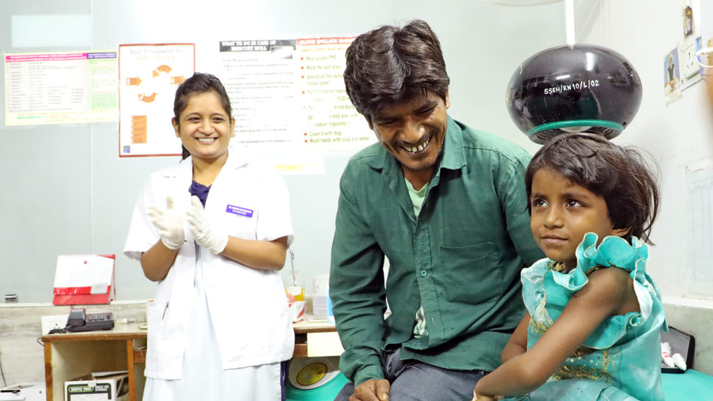 Rukmani sits with her father on a hospital bed.